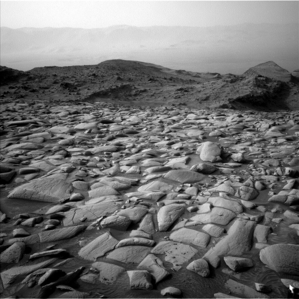Image taken by Mars rover Curiosity, with a rocky surface of Mars and hills from afar. 